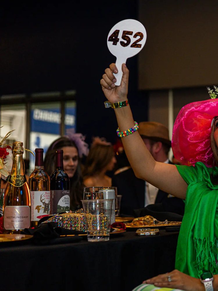 A guest in a pink derby hat raising bidding paddle number 452 during the paddle raise at the GiGi's Playhouse Indy gala.