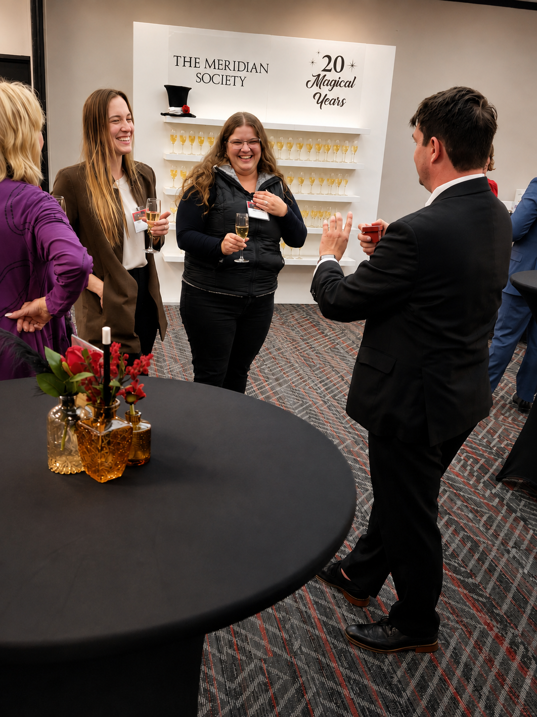 Josh Weidner performing close-up magic for guests at The Meridian Society twentieth anniversary reception, in front of a branded backdrop reading 20 Magical Years.