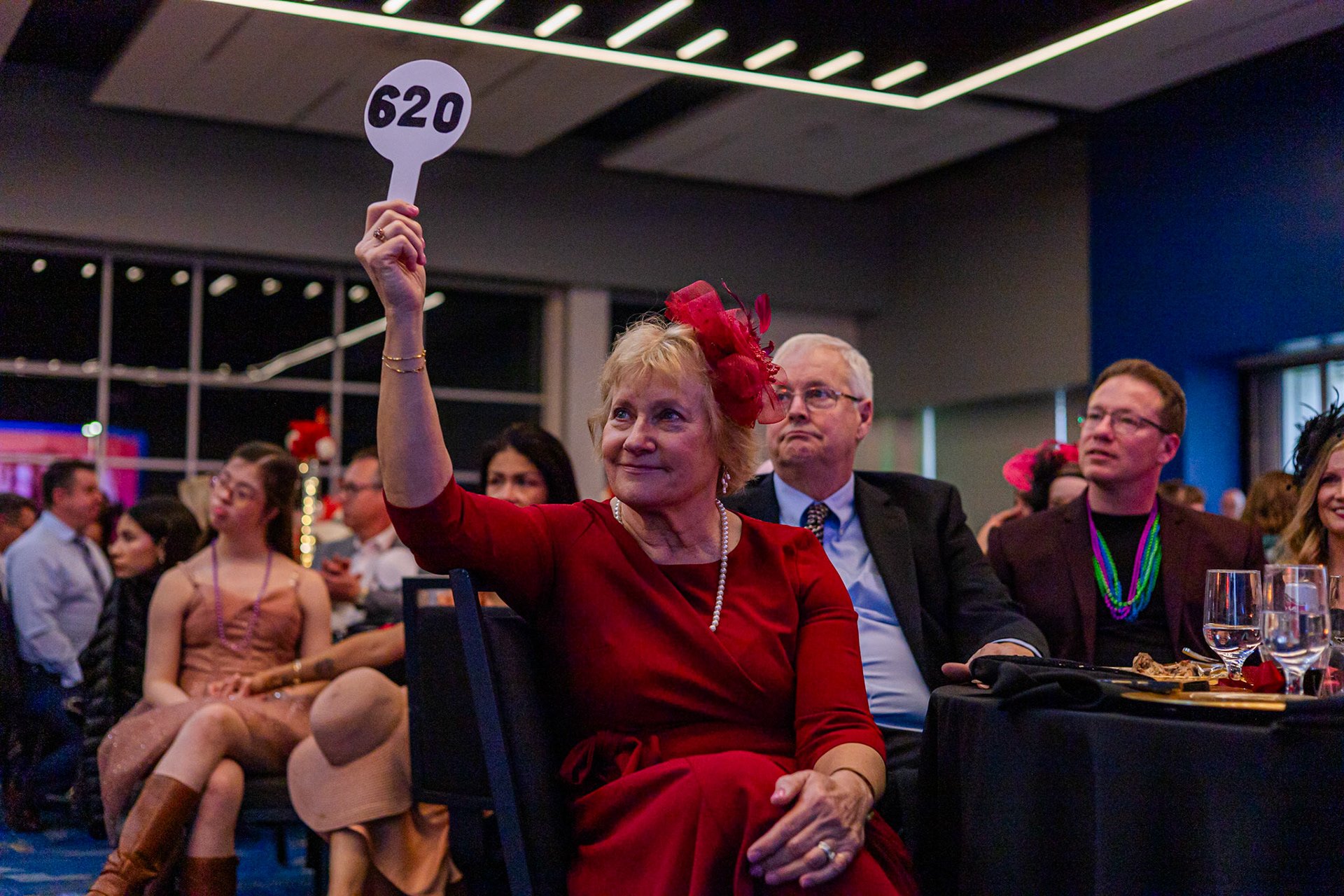A guest raising her bidding paddle during a fundraising gala paddle raise run by a corporate emcee