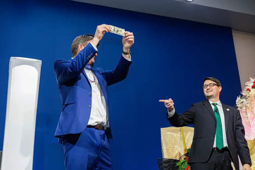 Corporate magician Josh Weidner hosting from the stage with a volunteer alongside him