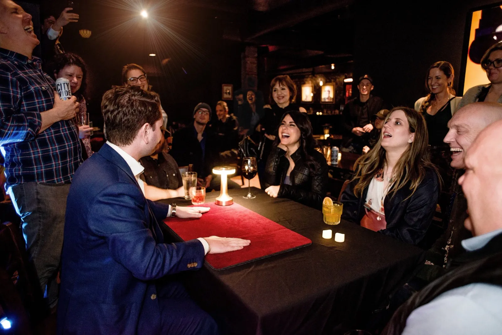 Guests gathered around the close up table laughing during the close up show at the St Louis magic show Disbelief: Cocktails and Conjuring